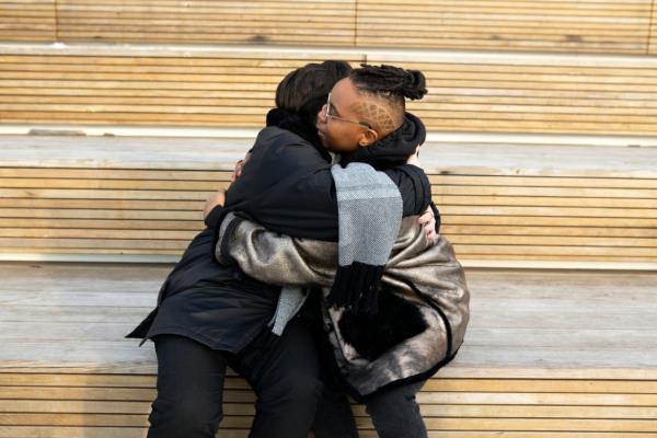 Two transmasculine friends embracing while sitting down